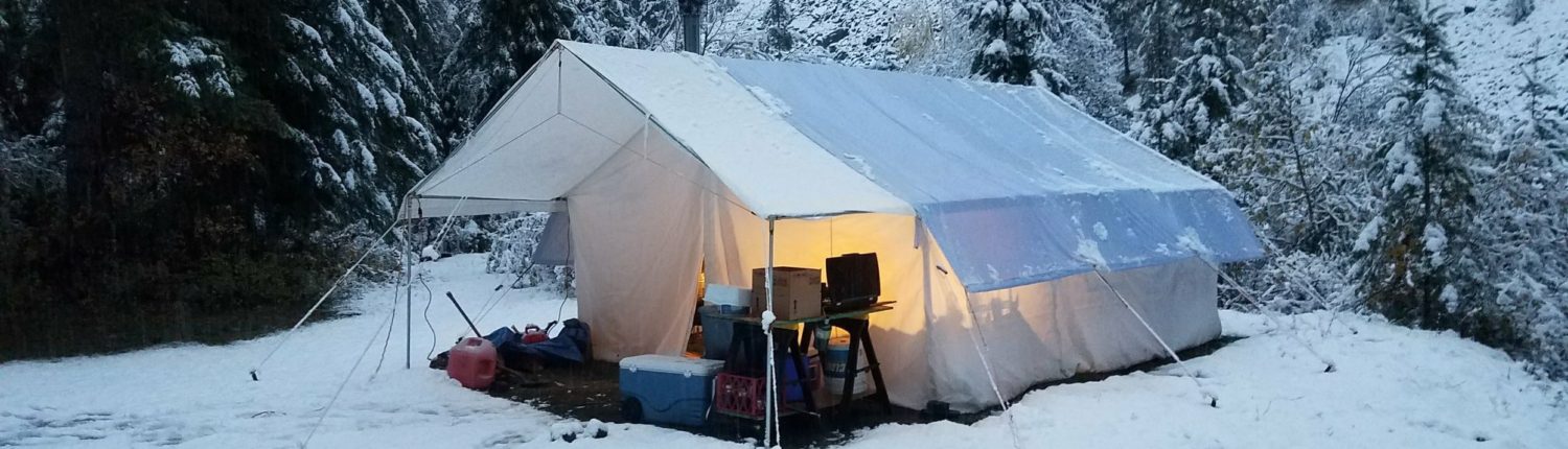 canvas wall tent in the snow with a stove and awning